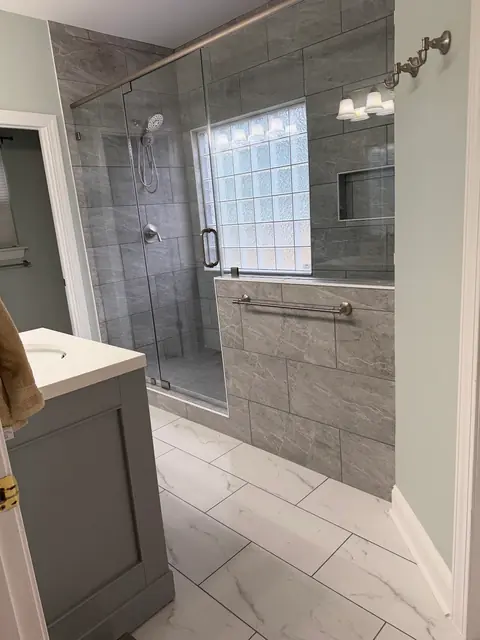 Glass-enclosed tile shower next to a gray vanity, with marble-look floor tile, from Amanda Stevens’s Google review
