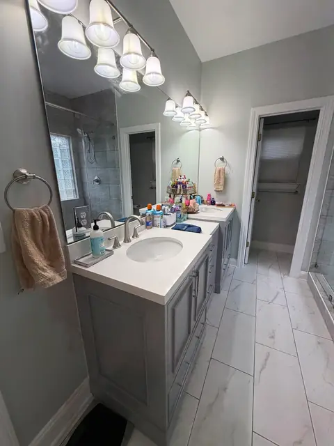 Double vanity with gray cabinets under a wide mirror and light bar, from Amanda Stevens’s Google review