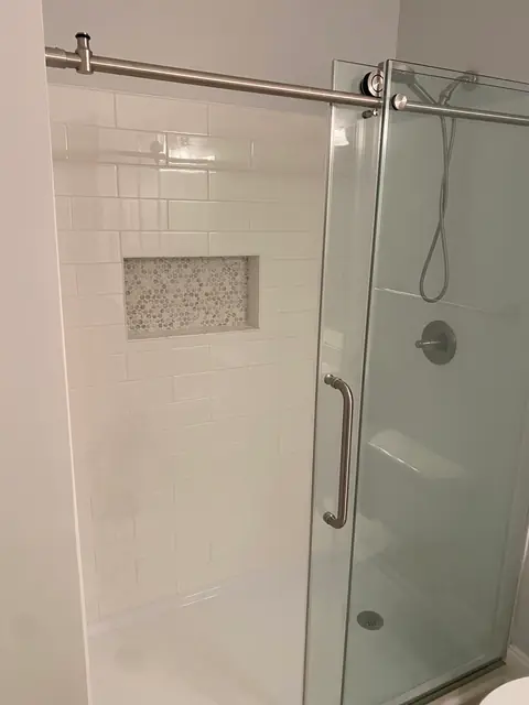 Glass sliding shower door, white wall tile and a mosaic niche, from Cole Wolcott’s Google review