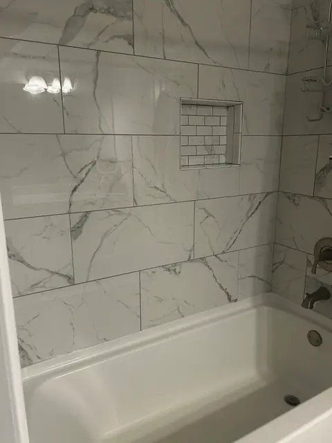 Tub with large marble-look wall tile and a tiled niche, from Kathleen Najar’s Google review